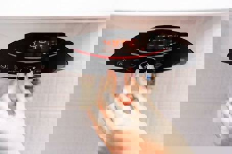 A person's hand adjusts the temperature knob on an electric water heater, with a digital display showing "44°C"